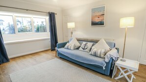 A bedroom with a blue sofa, patterned rug, and a painting on the wall. - Hafan Hapus (Beaumaris)