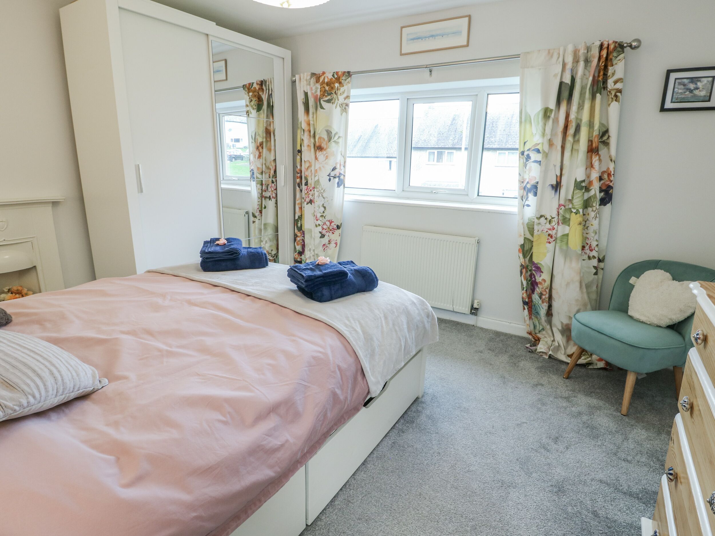 Um quarto com cama, cadeira, cômoda e janela com cortinas.
