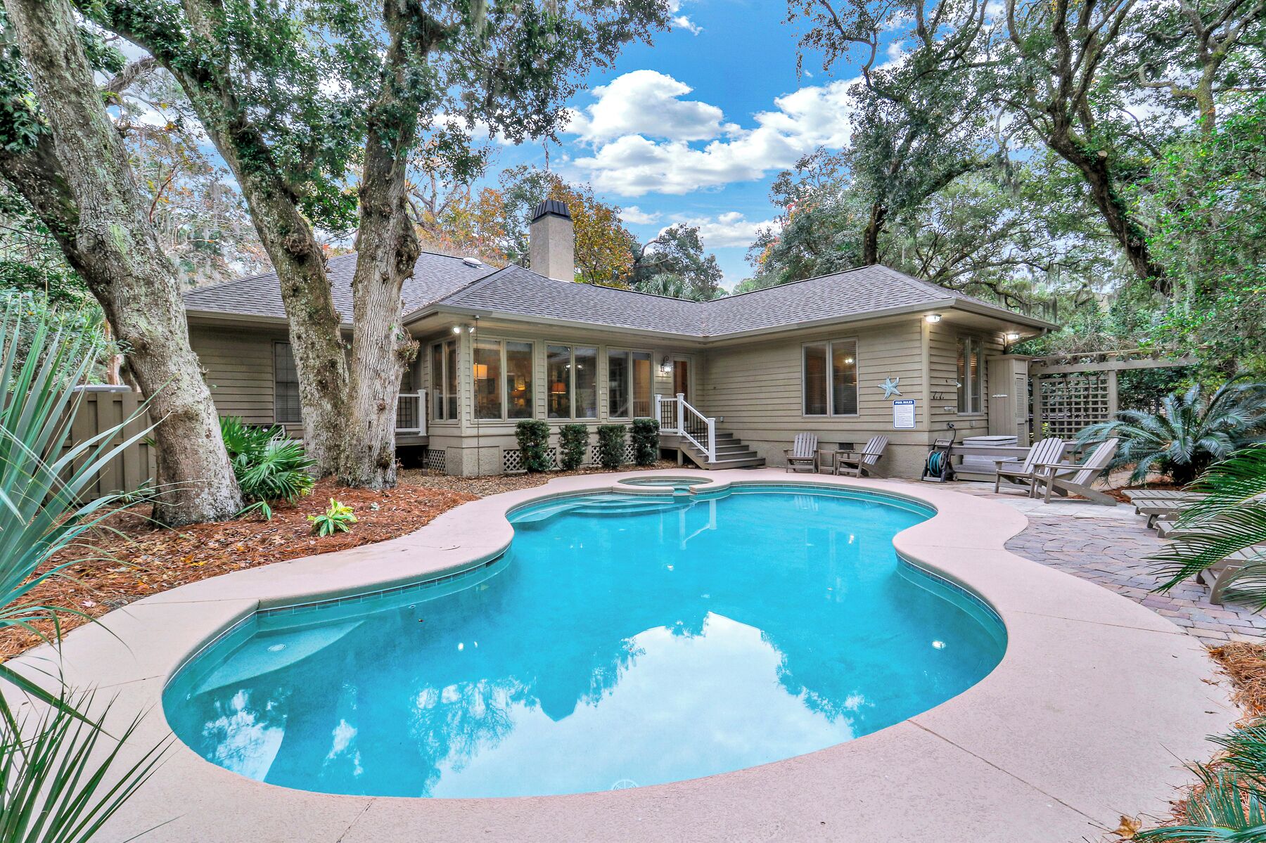 A house with a swimming pool surrounded by trees and a patio area with lounge chairs.