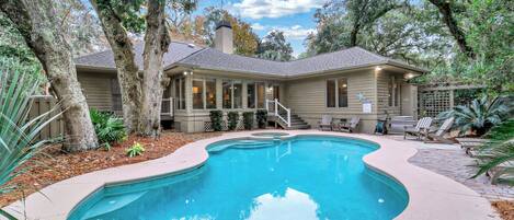 A house with a swimming pool surrounded by trees and a patio area with lounge chairs.