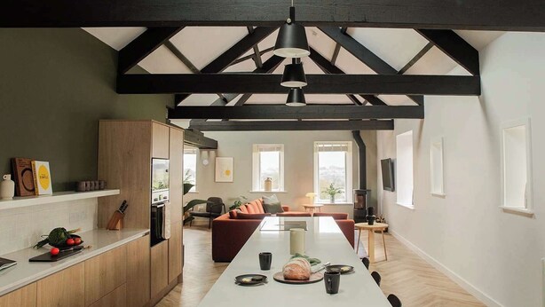 A spacious kitchen with a high ceiling and exposed beams, a central island, and a view into the living area.