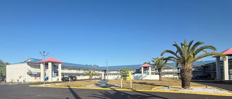 A building with multiple red-roofed structures, a parking lot, and palm trees.