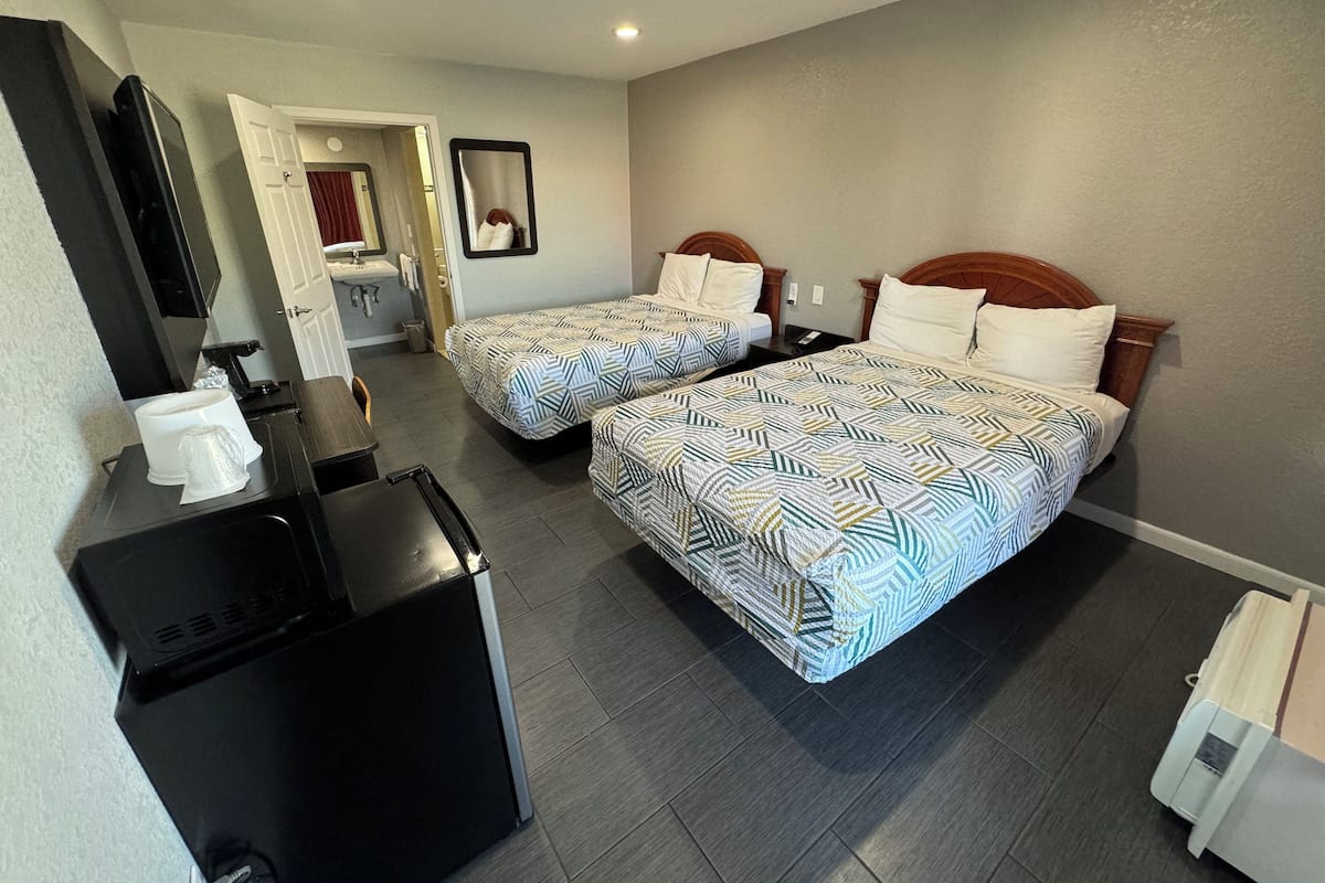 Habitación de hotel con dos camas, un escritorio, televisión y baño visible a través de una puerta abierta.