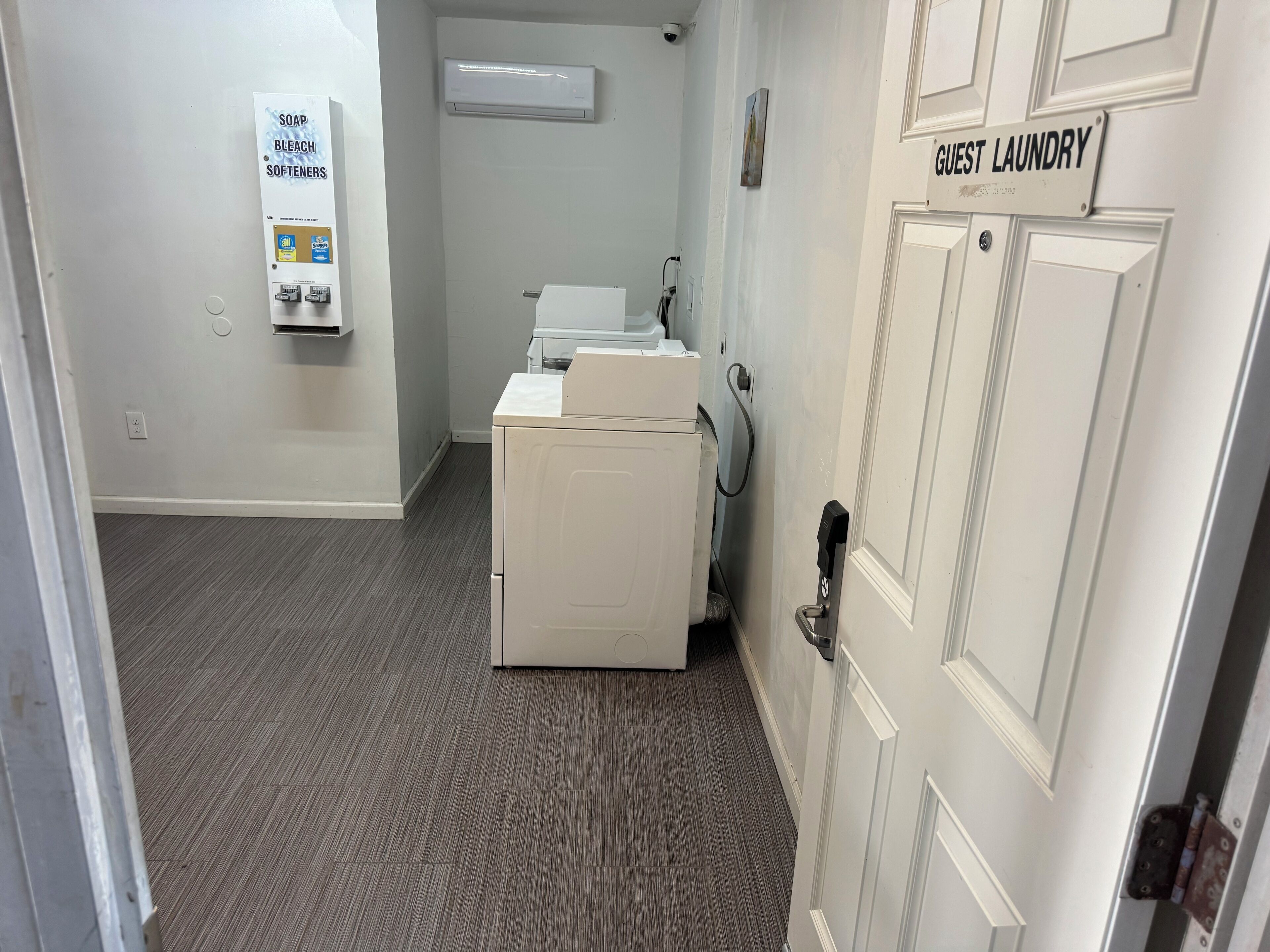 A laundry room with a sign indicating 'Guest Laundry' and a wall-mounted air conditioner.