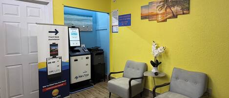A reception area with a desk, chairs, a computer, and a sign for front desk assistance.