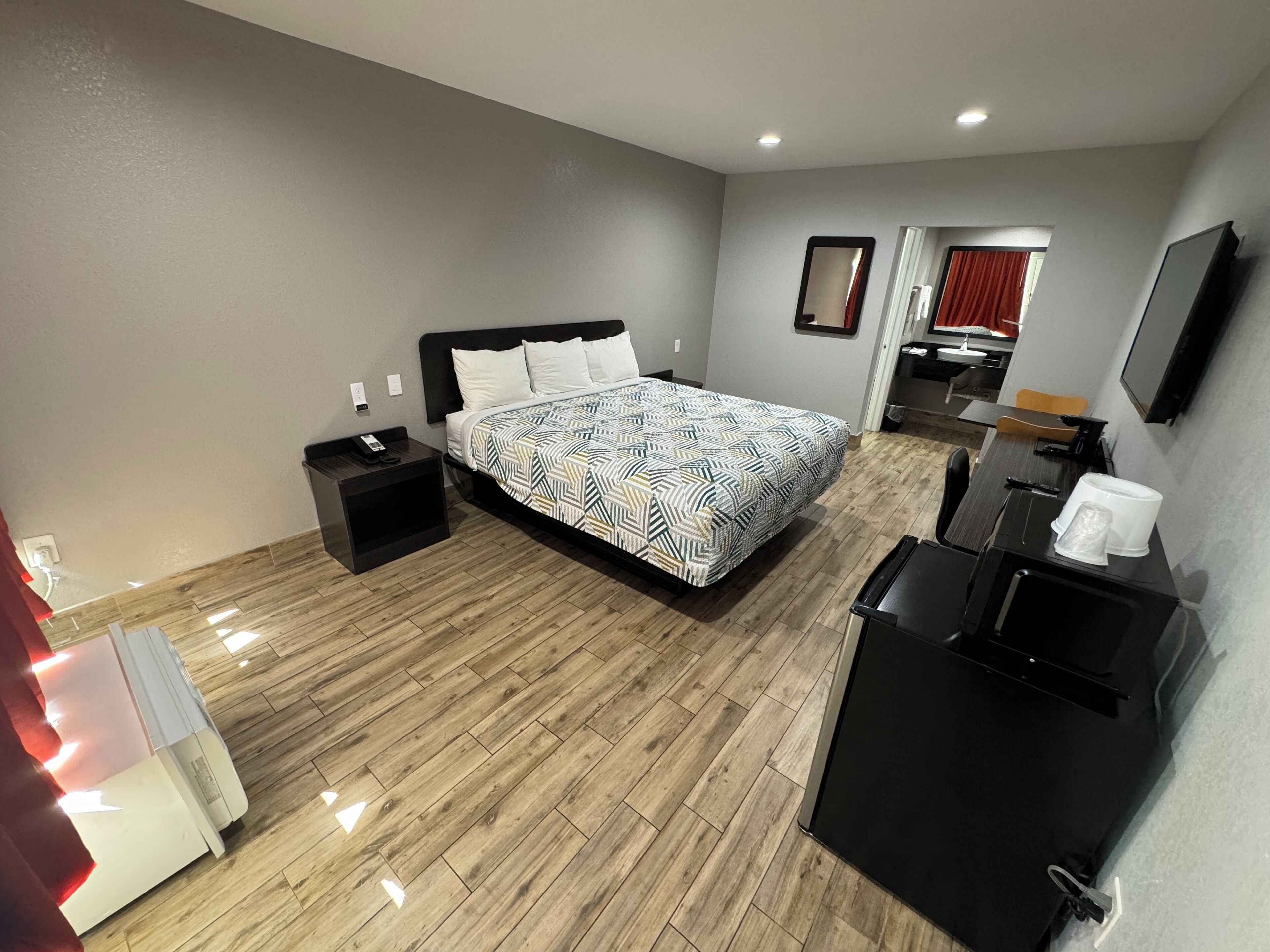 A hotel room with a bed, bedside tables, a desk, a chair, a TV, and a coffee machine.