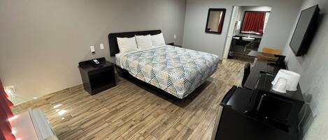 A hotel room with a bed, bedside tables, a desk, a chair, a TV, and a coffee machine.
