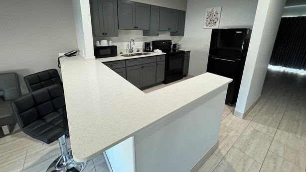 A modern kitchen with grey cabinets, a black refrigerator, and a white countertop. - Englewood Inn & Suites (Englewood)