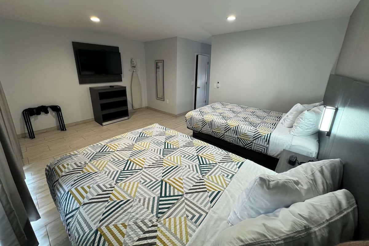 Habitación de hotel con dos camas, televisión, espejo y una pequeña zona de estar.
