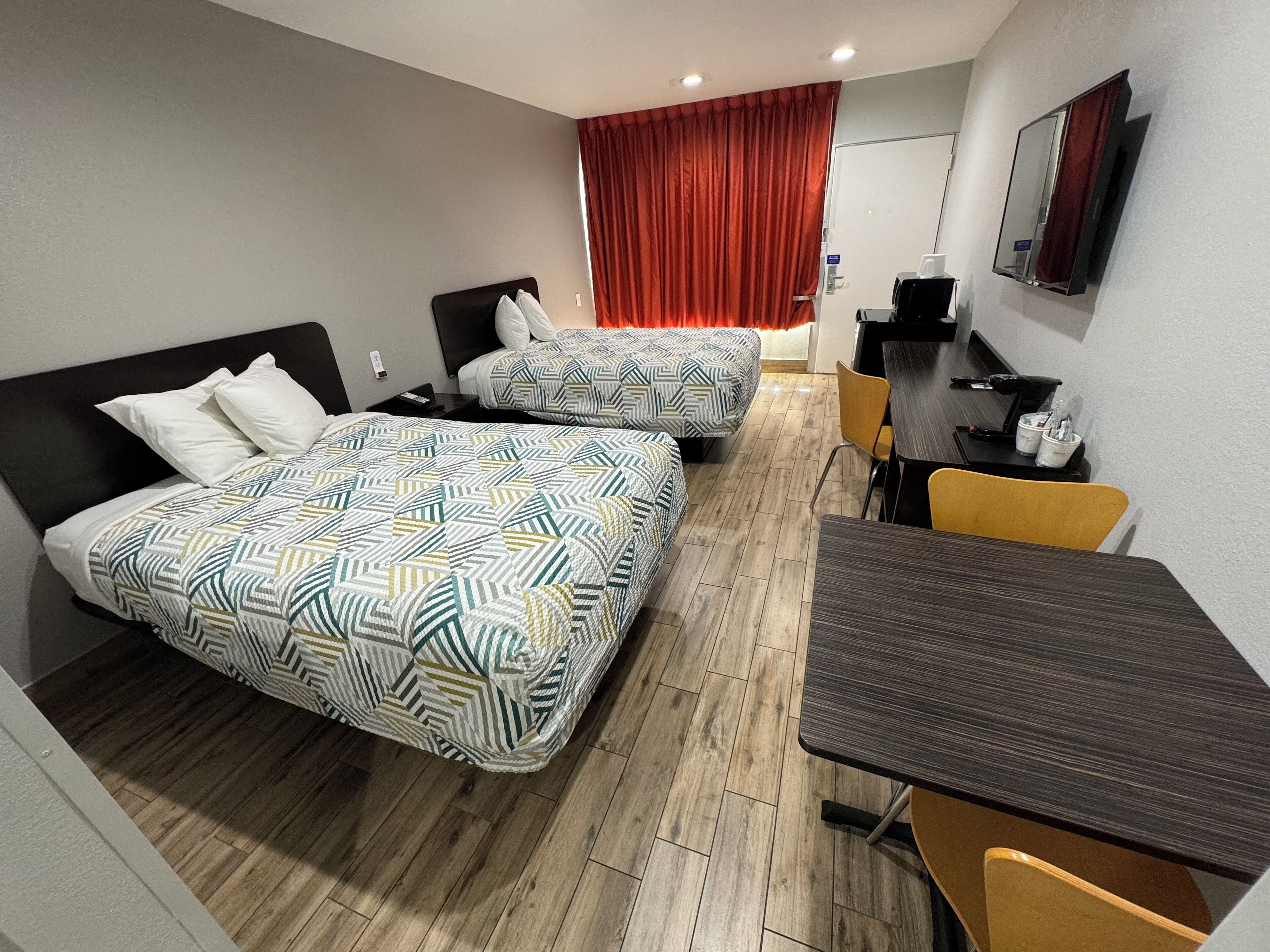 A hotel room with two beds, a desk, a chair, a TV, and a red curtain.