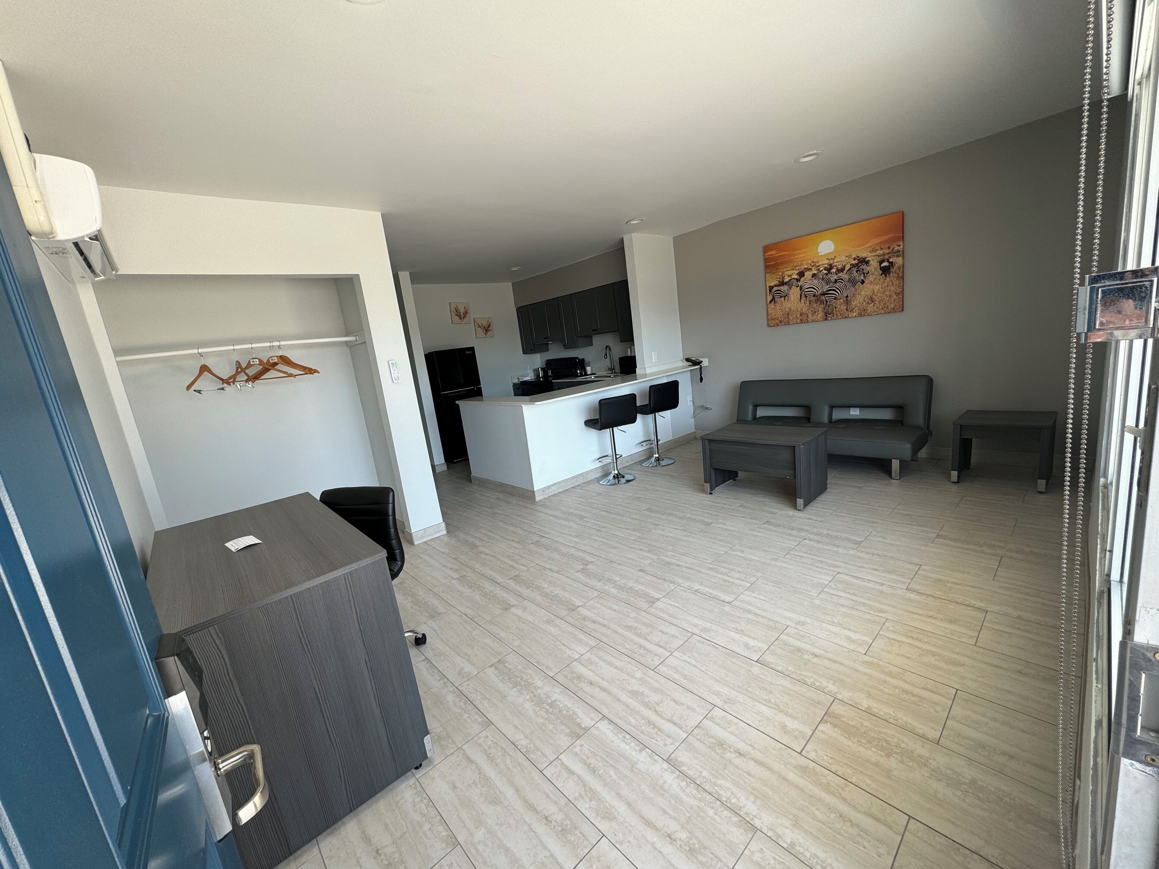 A modern living room with a grey sofa, a small coffee table, and a kitchen area with a white countertop and black appliances.