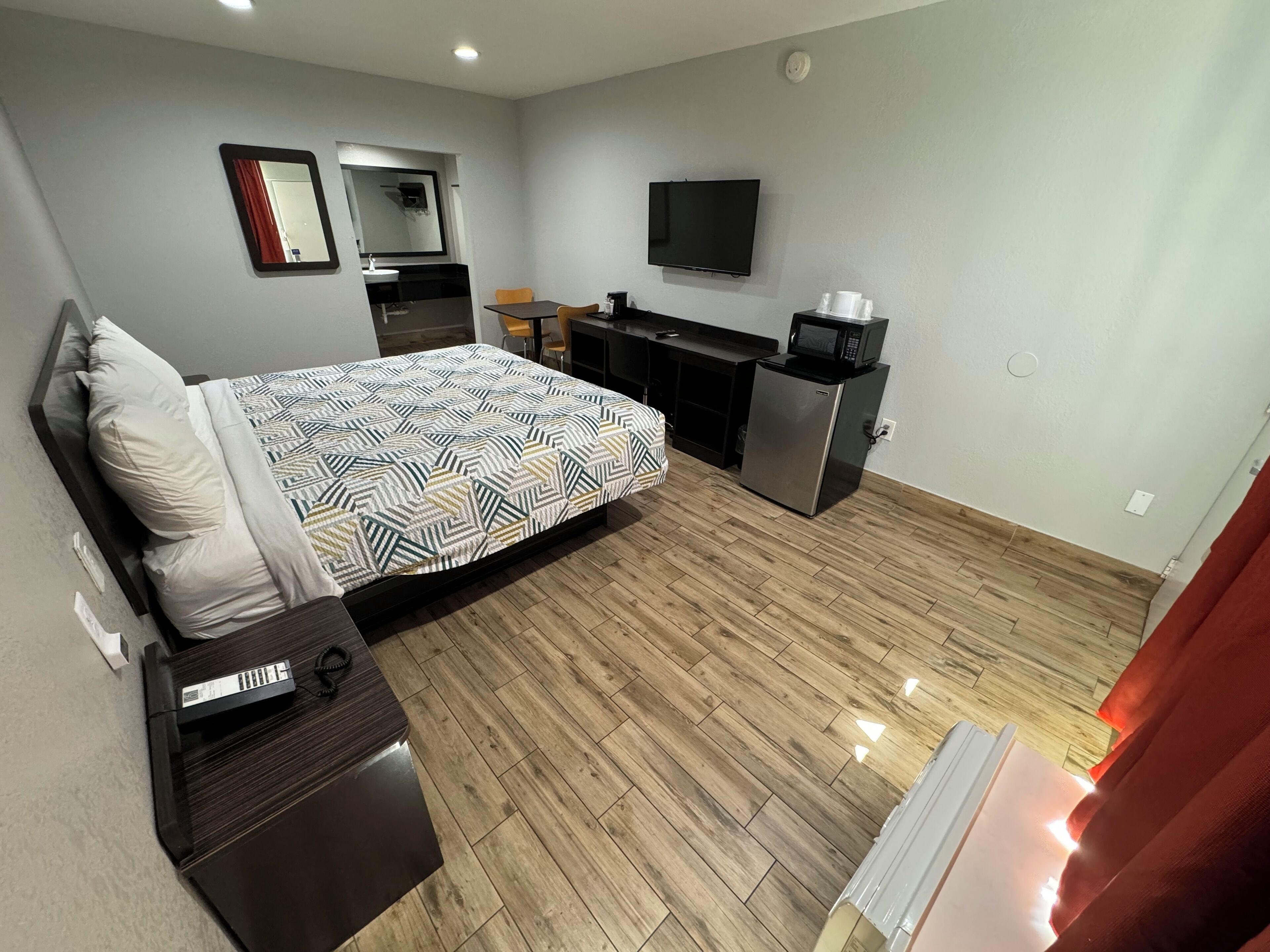 Quarto de hotel pequeno com uma cama, uma escrivaninha, um micro-ondas e uma televisão.