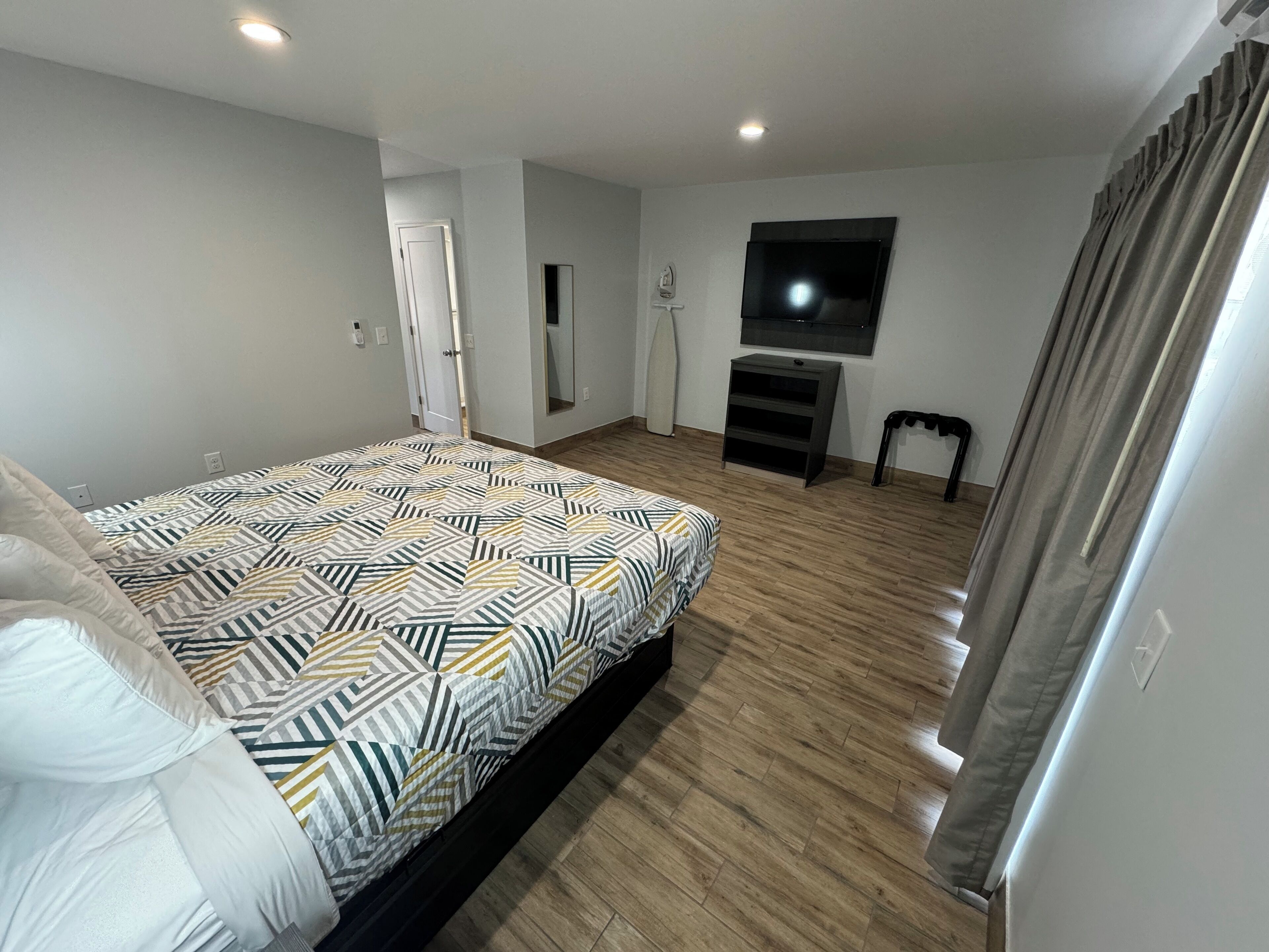 Une chambre à coucher avec un lit, un téléviseur fixé au mur, une petite table et une porte.