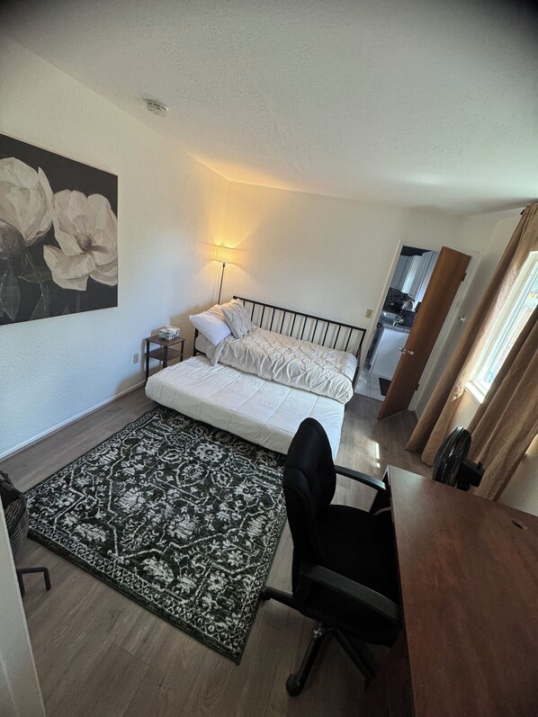 Un dormitorio con cama, escritorio, silla, lámpara, alfombra y un cuadro en la pared.