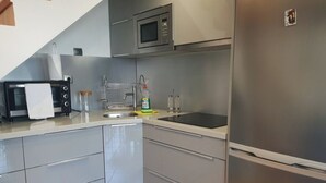 Una cocina moderna con armarios grises, un refrigerador de acero inoxidable, un microondas y un lavabo con una botella de detergente.