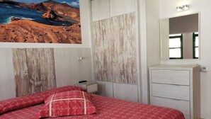 Un dormitorio con cama, cómoda, espejo e imagen en la pared de un paisaje costero.