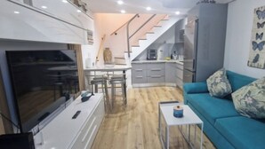 Un espacio habitable compacto con kitchenette, zona de comedor y área de estar con sofá y una pequeña mesa.