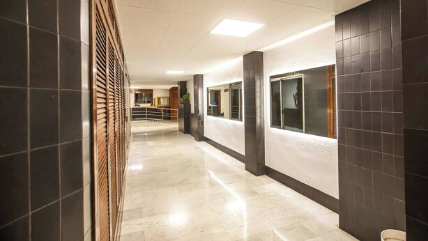A modern hotel corridor with a marble floor, dark wall panels, and a reception area in the distance. - Ebe1par1133- Apartment in Avenida Paralelo (Barcelona)