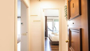 A hallway leading to a bedroom with a bed, a coat rack, and a door with a handle. - Ebe1par1133- Apartment in Avenida Paralelo (Barcelona)