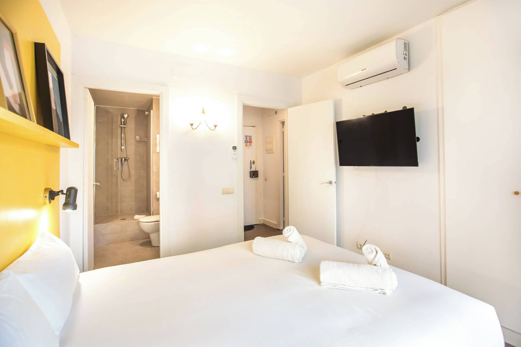 Een hotelkamer met een bed, douche, toilet en een wandtelevisie.