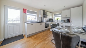 A modern kitchen with white cabinets, a dining area with a table set for four, and a view of the outside through the windows. - Paddington Lodge (Brigg)