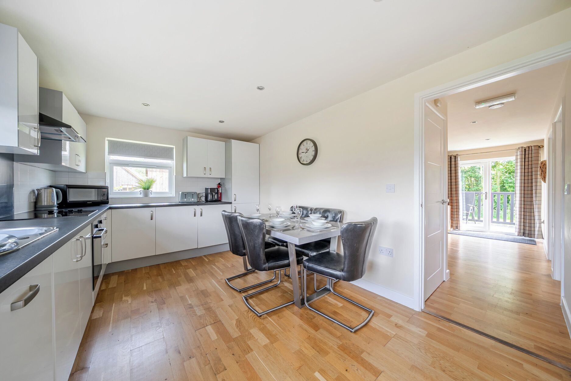 A modern kitchen with white cabinets, a dining table with four chairs, and a view to a balcony.