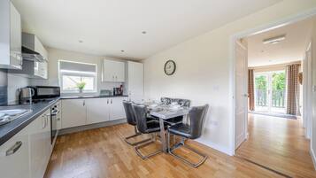 A modern kitchen with white cabinets, a dining table with four chairs, and a view to a balcony.