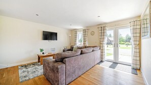 Ein Wohnzimmer mit einer Couch, einem Fernseher, einem Fenster mit Vorhängen und einem Holzboden.