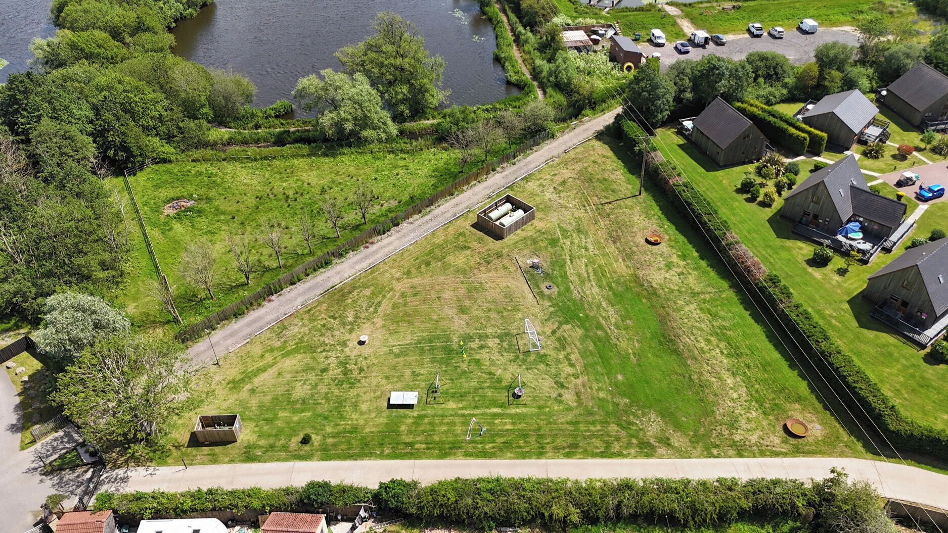 An aerial view of a residential area with houses, a grassy field, and a small building with tanks.