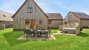A wooden building with a triangular roof, a door, and windows. There is a table with chairs in the front yard. - Lodge 2 - Charcoal (Brigg)