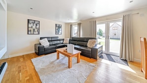 A modern living room with a black leather sofa, a wooden coffee table, and a large window with curtains. - Lodge 2 - Charcoal (Brigg)