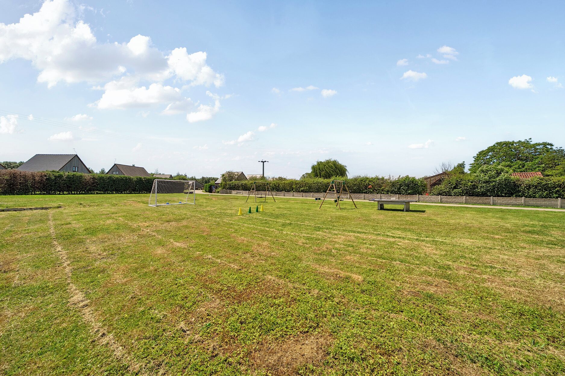 A grassy field with a soccer goal, swings, and a bench.