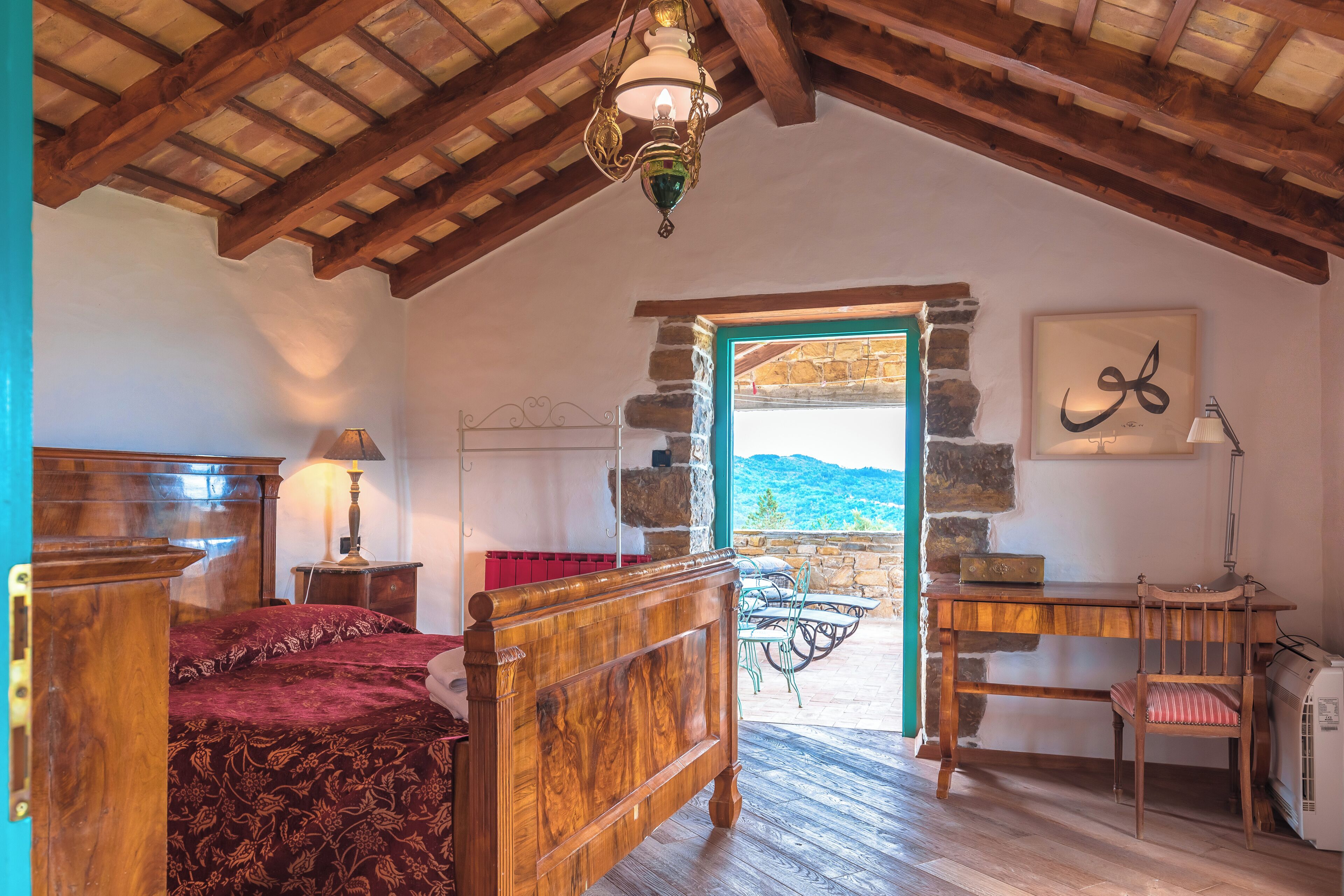 A bedroom with a wooden bed, a desk, a chair, and a stone wall.