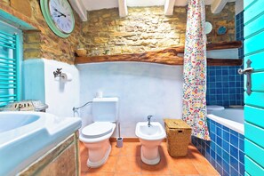 A bathroom with a stone wall, a blue bathtub, a white toilet, a white sink, and a bidet. - STANCIJA SANCTA MARIA - HERITAGE  WELLNESS RETREAT (Oprtalj)