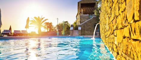 A swimming pool with clear water, a stone wall, and a building with a balcony.