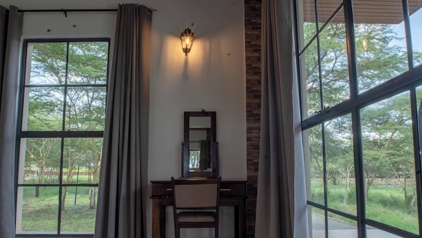 Een kamer met een bureau en stoel, grote ramen met gordijnen, een wandlamp en een accentmuur van baksteen.
