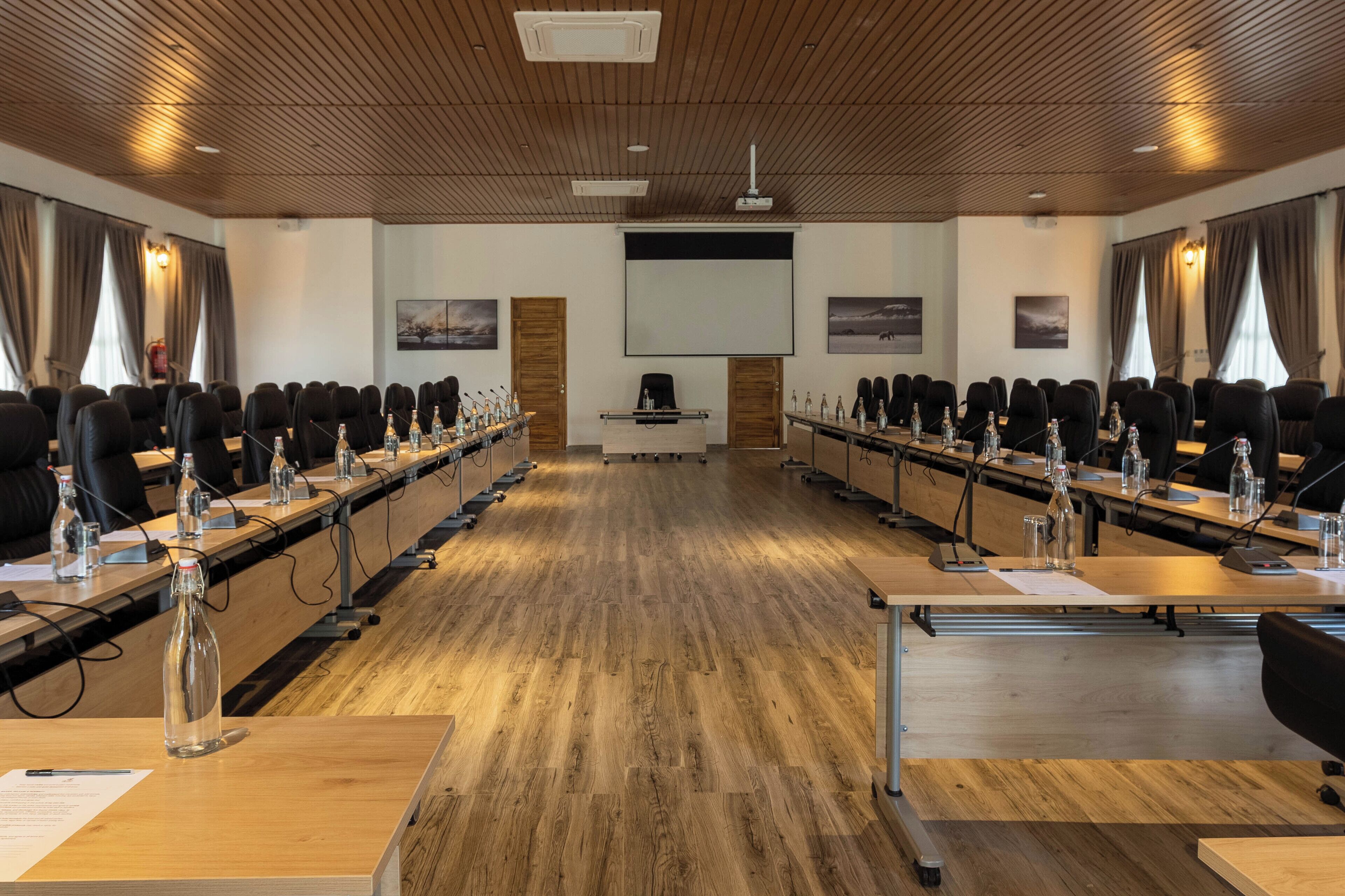 Konferenssitila, jossa on pitkiä pöytiä, mikrofoneja ja kannettavia tietokoneita.