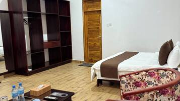 A hotel room with a bed, a wooden wardrobe, a desk with a telephone, and two floral armchairs.