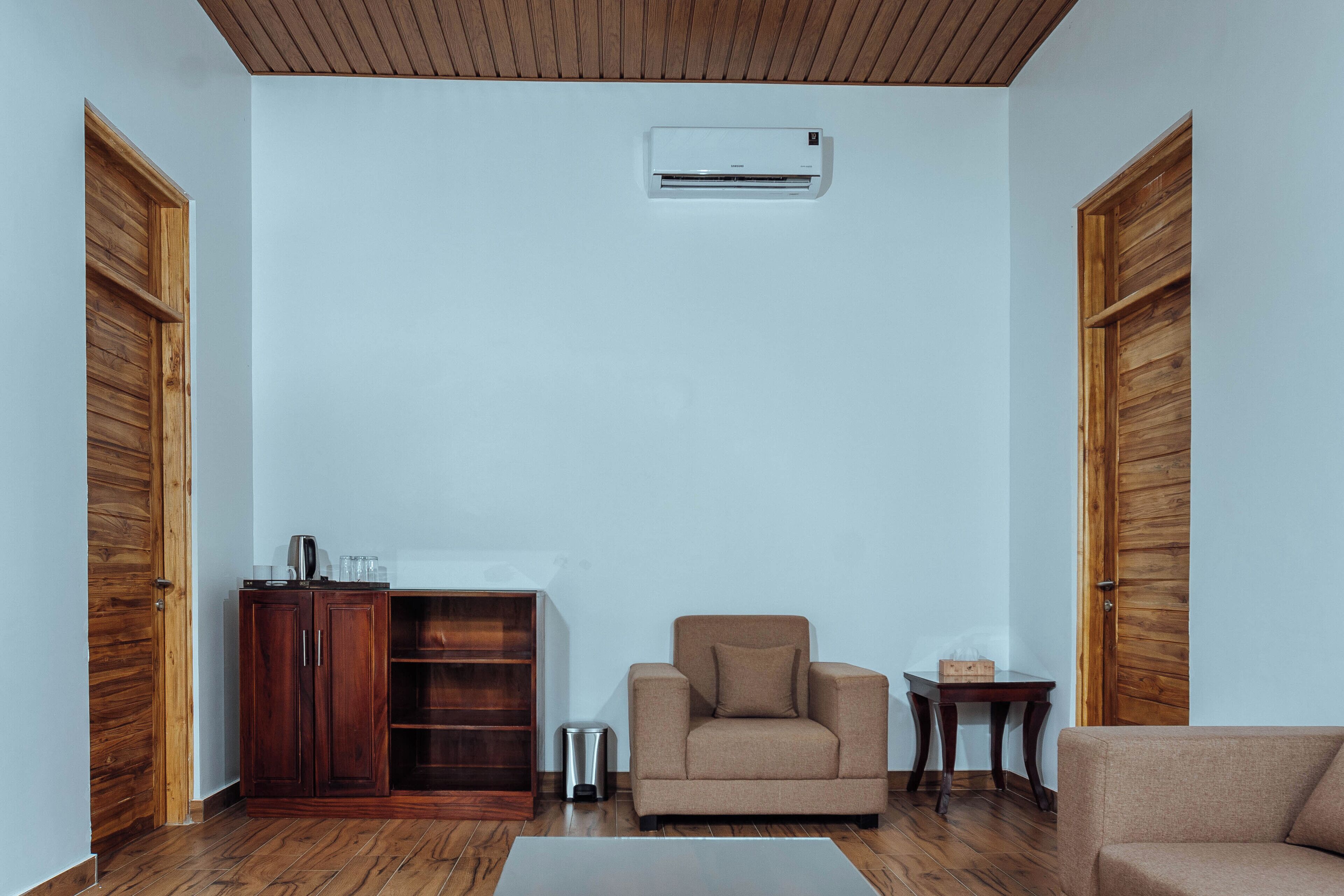 Une pièce avec un plafond en bois, un mur blanc, un canapé beige, un meuble en bois, une petite poubelle et une table sur laquelle se trouve une boîte.