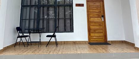 Ein Zimmer mit großem Fenster, Holztür und kleinem Tisch mit zwei Stühlen.