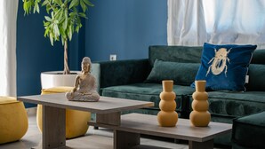 Une pièce comprenant une statue de méditation posée sur une table, une plante en pot, un canapé vert et deux vases.