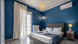 Une chambre avec un grand lit, une table de chevet avec une lampe, une fenêtre avec des rideaux et un appareil de climatisation fixé au mur.