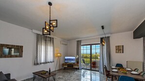 Un salon comprenant un canapé, un téléviseur, une table à manger avec des chaises et une grande fenêtre avec des rideaux.