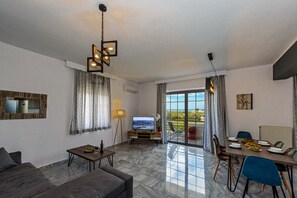 Una sala de estar con sofá, televisión, mesa de comedor con sillas y un ventanal con cortinas.