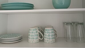 A shelf with teal plates, a teal bowl, patterned mugs, and clear glasses. - Kasa y Familia 811 (Valdivia)