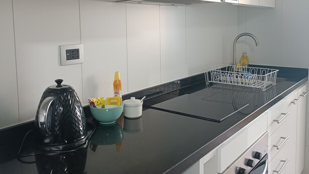 A modern kitchen with white cabinets, a black countertop, a microwave, and a dish rack. - Kasa y Familia 811 (Valdivia)