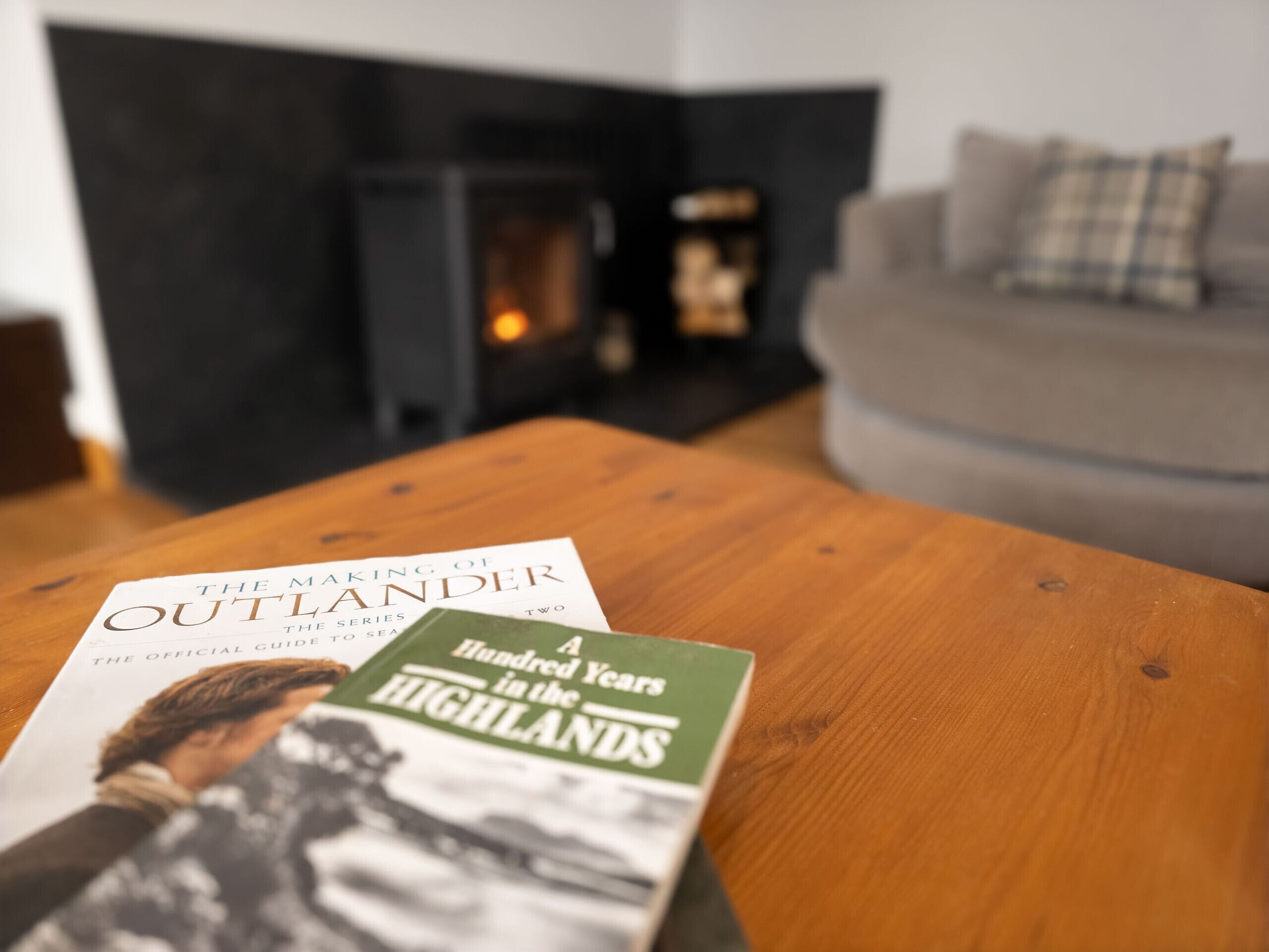 Een boek met de titel 'The Making of Outlander' en 'A Hundred Years in the Highlands' op een houten tafel.
