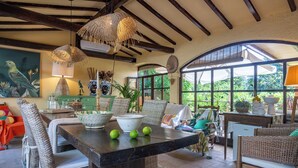 A spacious room with a dining table, wicker chairs, and a large window providing a view of greenery. - Podere la Botte Pool Lari (Lari)