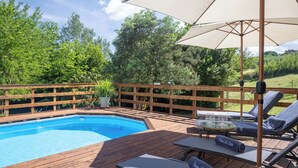 Een houten terras met een zwembad, ligbedden en parasols.
