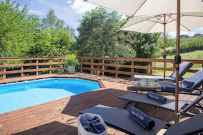 Een houten terras met een zwembad, ligbedden en parasols.